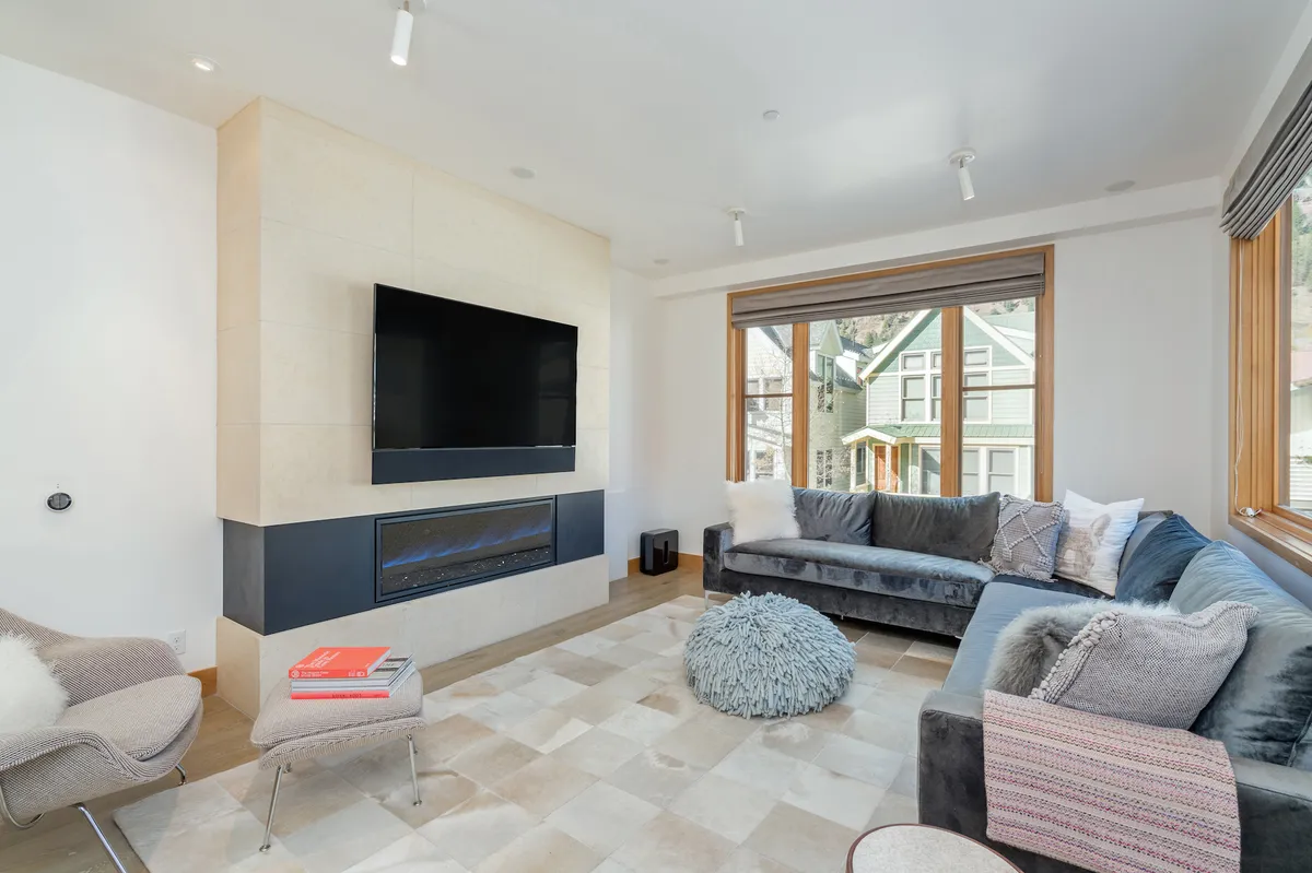 A cozy living area centered around a fireplace, with a plush sofa facing a large window that frames the outdoors. The scene is set for a movie night or a cozy evening by the fire—perfect for après-ski storytelling or quiet relaxation.
