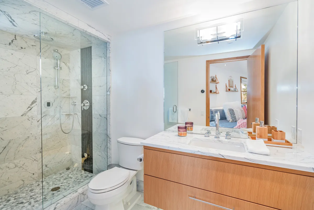 A spa-inspired bathroom with a glass shower enclosure, marble countertop, and wood cabinetry. The serene environment and natural light reinforce the idea of relaxation and indulgence.