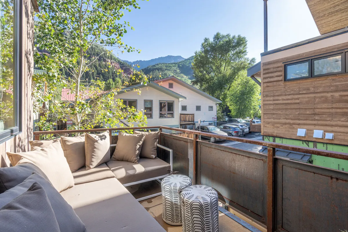 This scene shows a comfortable outdoor seating area on a deck or balcony, surrounded by greenery and with expansive mountain views. Decorative stools and relaxed seating create a tranquil, inviting atmosphere, ideal for lounging or hosting small gatherings.