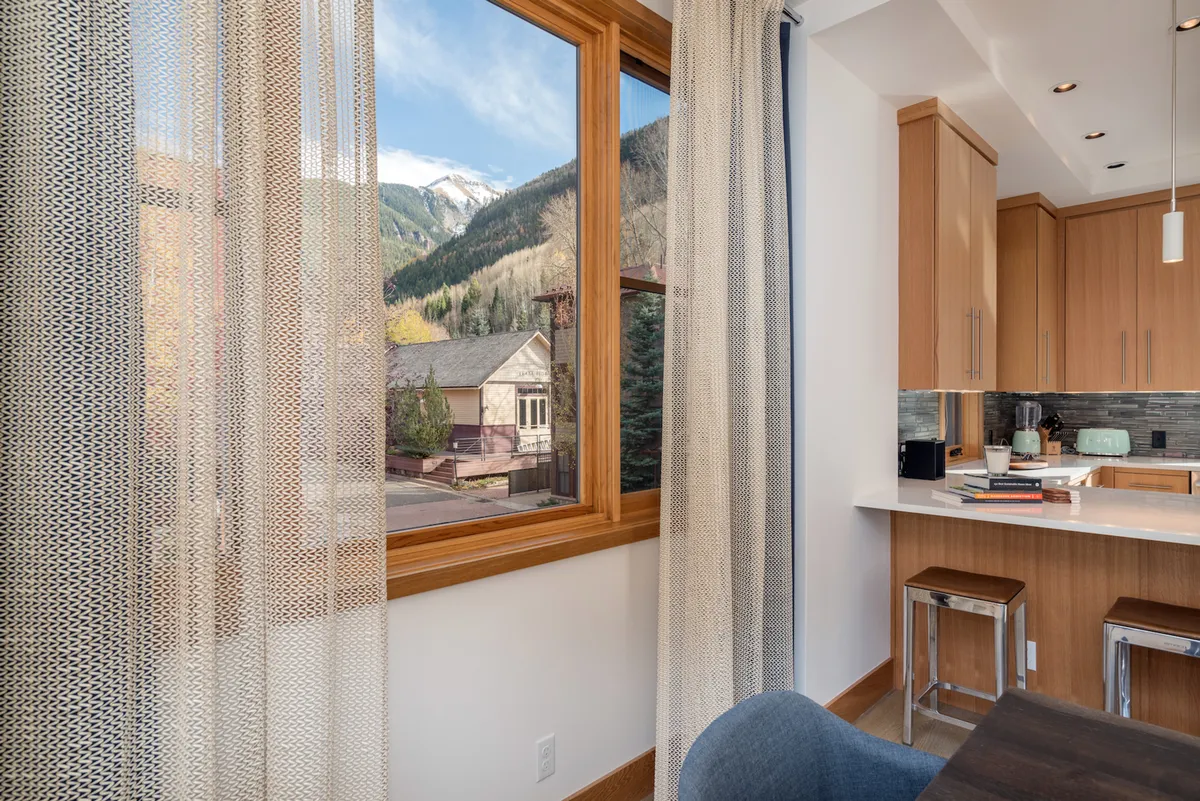 A sunlit kitchen interior with a large window framing majestic mountain views, a spacious counter, and cozy dining area. The scene invites post-adventure meals and warm gatherings with friends or family.