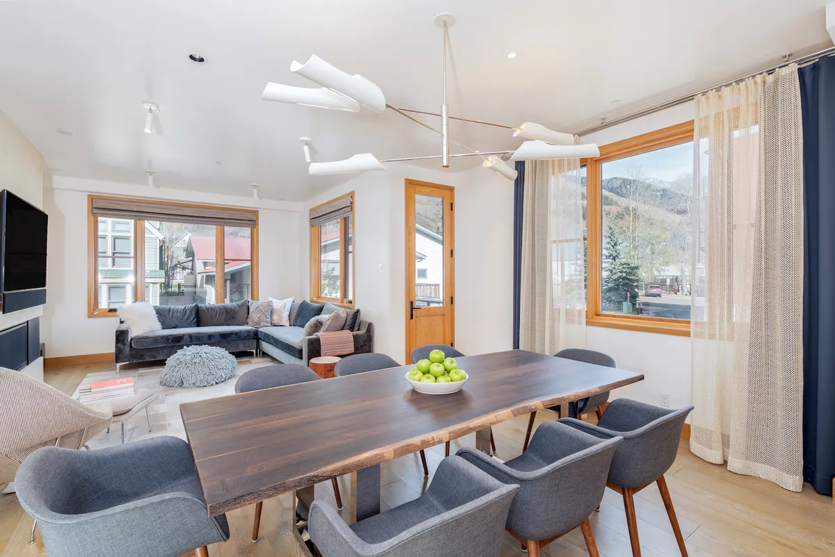 A sunlit interior scene with a welcoming dining table decorated with green apples, a comfortable couch, and large windows that flood the space with natural light. The setting is perfect for family meals, social gatherings, and quiet relaxation.