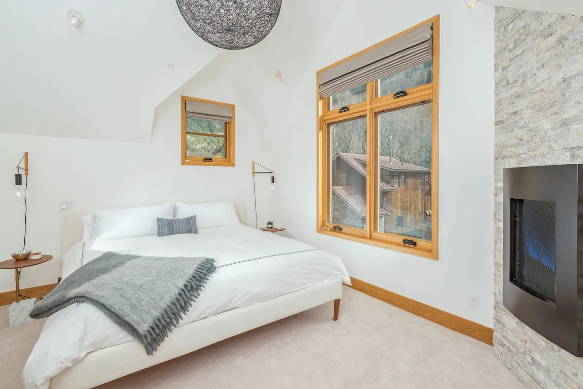 A serene master bedroom featuring a king-sized bed, a cozy fireplace, and ample windows letting in natural light. The space exudes warmth and comfort, emphasizing privacy and an inviting retreat-like atmosphere.