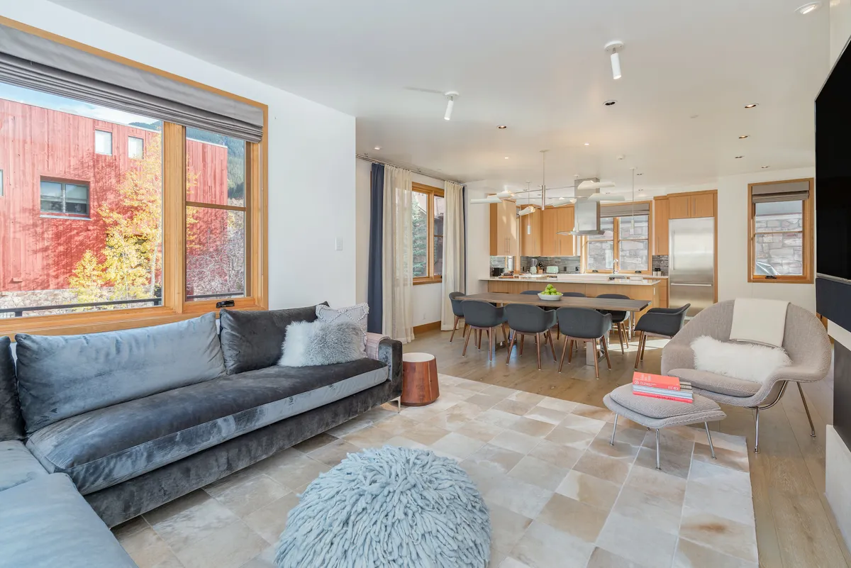 A stylish interior shot featuring a plush sofa, spacious dining table, kitchen island, and expansive windows letting in natural light. The ambiance is both comfortable and modern, ideal for family dinners, dinner parties, or relaxing with friends. The layout encourages interaction and shared experiences.